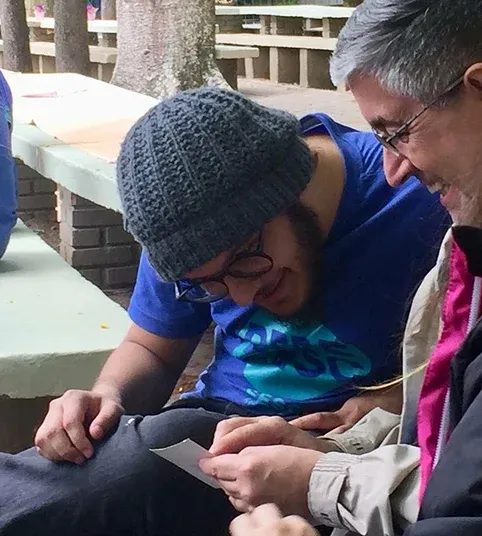 Bruno in a knit beanie, laughing over a card with a colleague.